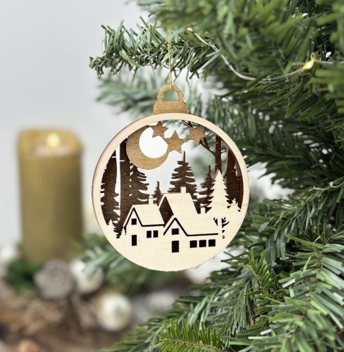 Runder Christbaumschmuck aus Holz mit winterlichem Dorf, Tannenwald, Mond und Sternen, aufgehängt an einem grünen Weihnachtsbaum.