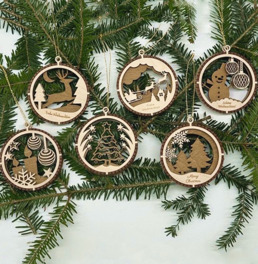Sechs runde Holz Weihnachtsanhänger in 3D-Optik mit Hirsch, Schlitten, Schneemann, Kerzen und Tannenbäumen auf grünen Zweigen – vielfältige Ideen für Weihnachtsbaumschmuck und rustikale Weihnachtsdeko aus Holz.