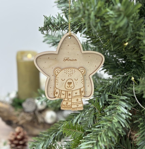 Personalisierter Holz Weihnachtsanhänger in Sternform mit dem Namen Florian, graviertem Bären und gemustertem Schal, an einem Christbaum mit Kerze, Zapfen und Weihnachtsdekoration.
