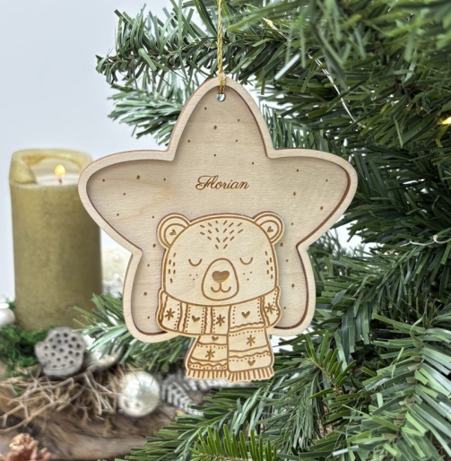 Frontal fotografierter Holz Weihnachtsanhänger in Sternform mit dem Namen Florian, graviertem Bären, gemustertem Schal und kleinen Sternen, festlich am grünen Christbaum aufgehängt.