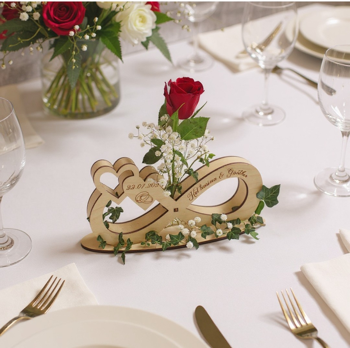 Unendlichkeitszeichen aus Holz mit Namen Katharina & Günther, Datum und Ringen graviert, mit roter Rose im Blumenröhrchen auf einer festlich gedeckten Hochzeitstafel